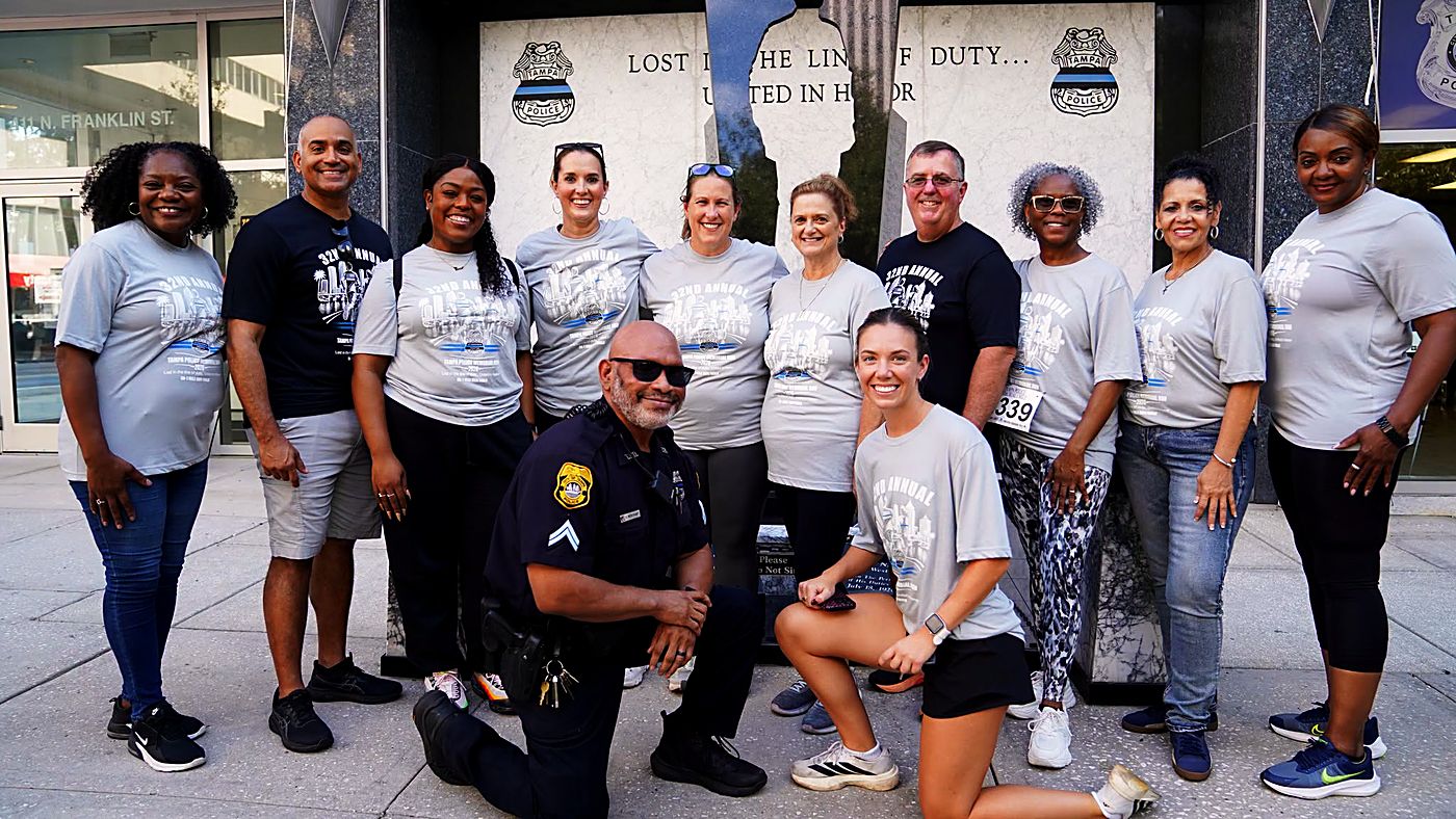 A group of runners and a Tampa Police officer kneeling together at the memorial monument