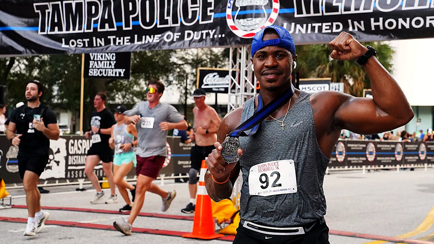 A runner flexing and showing his finisher medal at the Memorial Run finish-line banner